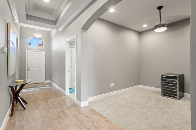 foyer entrance with wine cooler, an inviting chandelier, light hardwood / wood-style floors, and ornamental molding