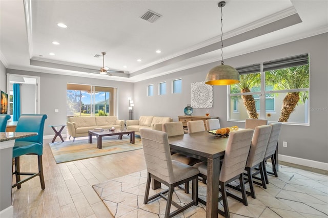 dining space with light wood-type flooring, a tray ceiling, ceiling fan, and ornamental molding