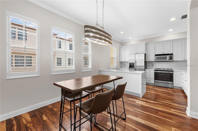 kitchen with hardwood / wood-style flooring, stainless steel appliances, hanging light fixtures, white cabinets, and decorative backsplash