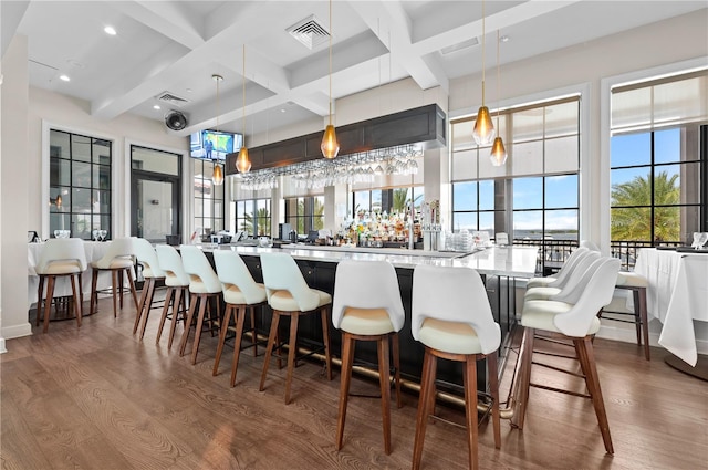 bar with beam ceiling, hardwood / wood-style flooring, decorative light fixtures, and coffered ceiling