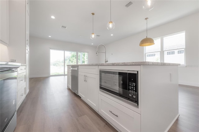 kitchen with white cabinetry, stainless steel range oven, pendant lighting, a center island with sink, and light wood-type flooring