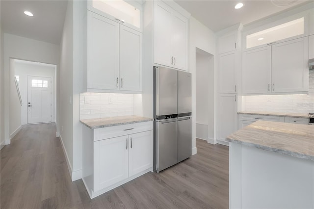 kitchen with light hardwood / wood-style floors, white cabinetry, stainless steel refrigerator, and light stone counters