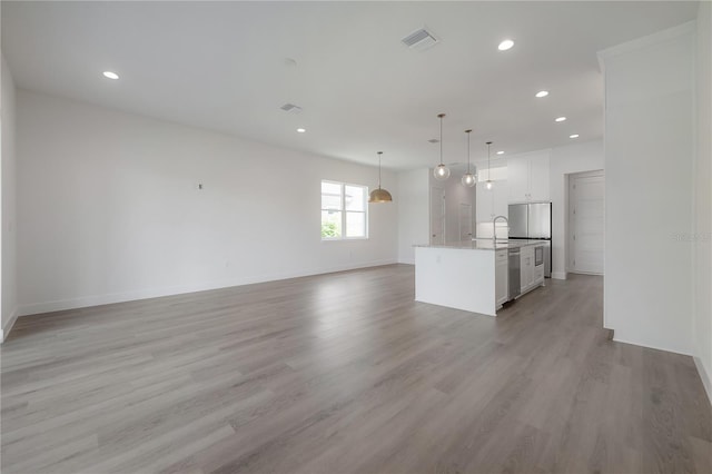 kitchen featuring light hardwood / wood-style flooring, an island with sink, white cabinets, decorative light fixtures, and sink