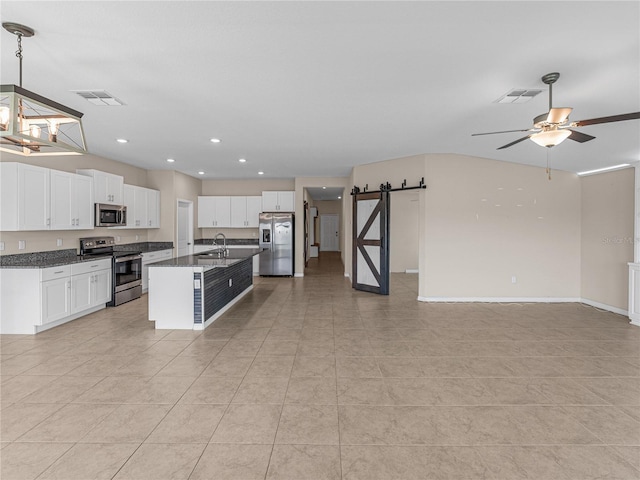 kitchen with stainless steel appliances, a barn door, a kitchen island with sink, and white cabinets