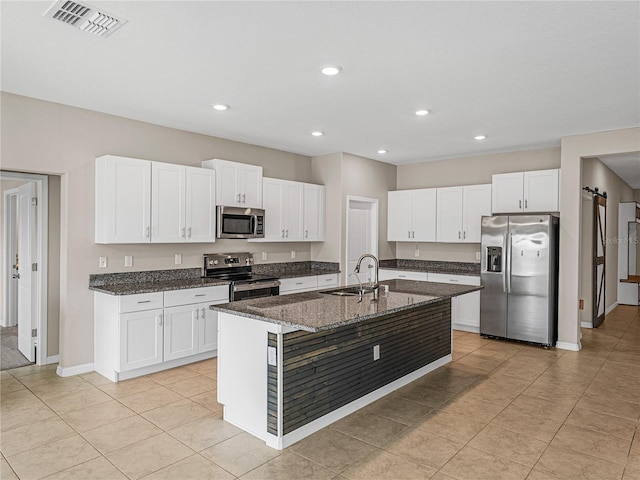 kitchen featuring sink, appliances with stainless steel finishes, white cabinetry, a center island with sink, and dark stone counters