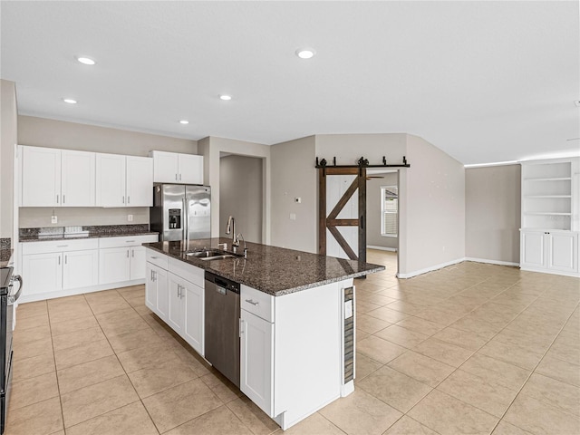 kitchen featuring sink, dark stone countertops, appliances with stainless steel finishes, an island with sink, and a barn door