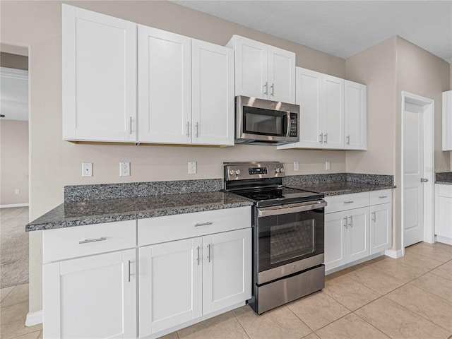 kitchen with white cabinetry, light tile patterned floors, stainless steel appliances, and dark stone counters