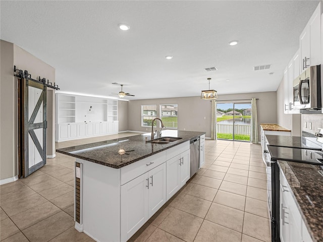 kitchen with sink, appliances with stainless steel finishes, a kitchen island with sink, white cabinets, and a barn door