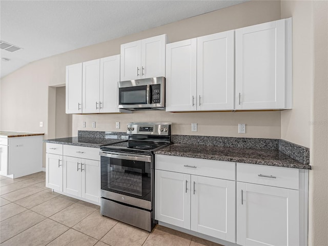 kitchen featuring white cabinetry, appliances with stainless steel finishes, dark stone countertops, and light tile patterned flooring