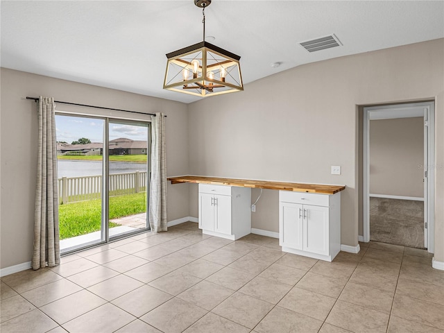 unfurnished dining area with built in desk, an inviting chandelier, and light tile patterned floors