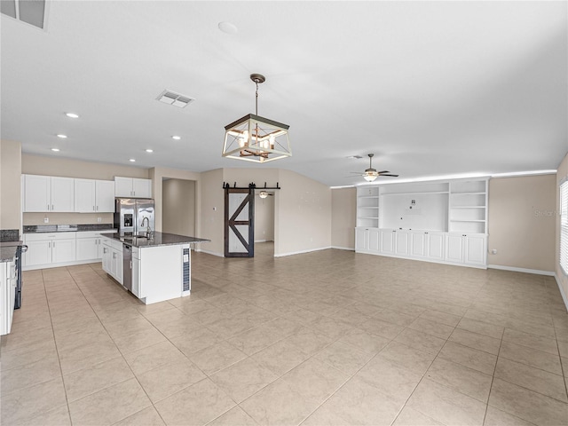 kitchen with built in features, white cabinets, hanging light fixtures, a barn door, and a center island with sink