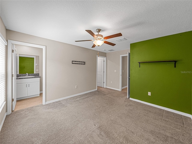 unfurnished bedroom featuring sink, ceiling fan, ensuite bathroom, a textured ceiling, and light carpet