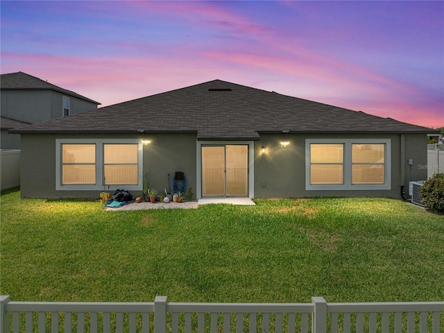 back house at dusk with central AC and a lawn