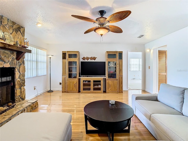 living room with light hardwood / wood-style floors, a fireplace, ceiling fan, and a textured ceiling