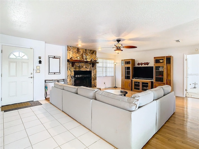 unfurnished living room featuring light hardwood / wood-style floors, a textured ceiling, a stone fireplace, and ceiling fan