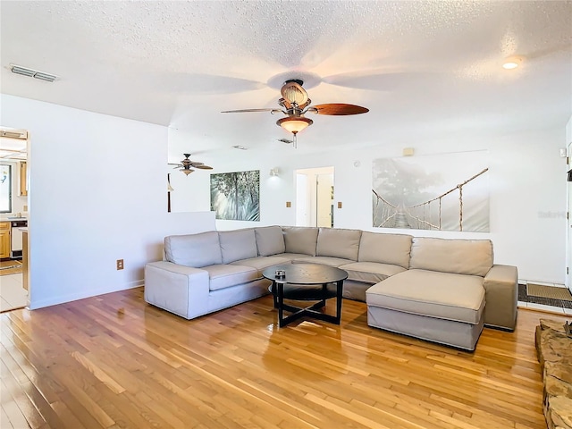 living room with a textured ceiling, light wood-type flooring, and ceiling fan