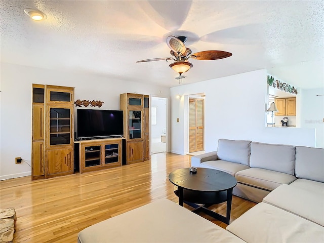 living room with light hardwood / wood-style floors, a textured ceiling, and ceiling fan