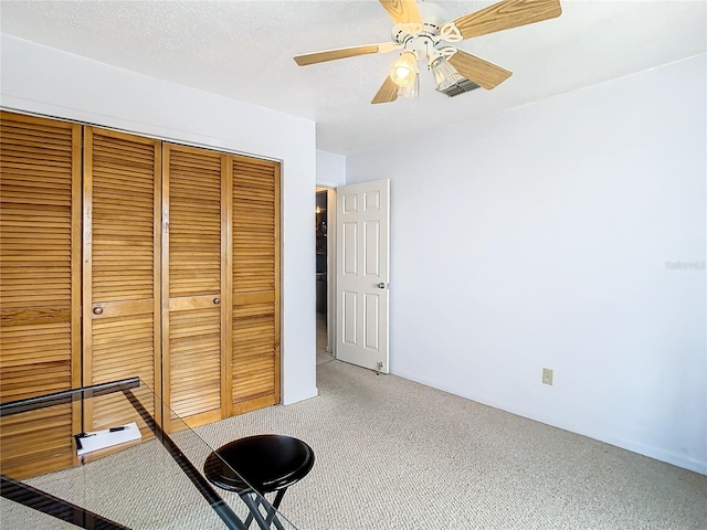 unfurnished bedroom featuring a textured ceiling, carpet, a closet, and ceiling fan