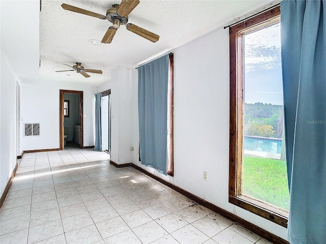 spare room with a textured ceiling, light tile patterned floors, and ceiling fan