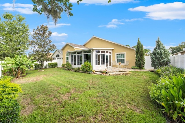 back of property with a sunroom, a lawn, and a patio