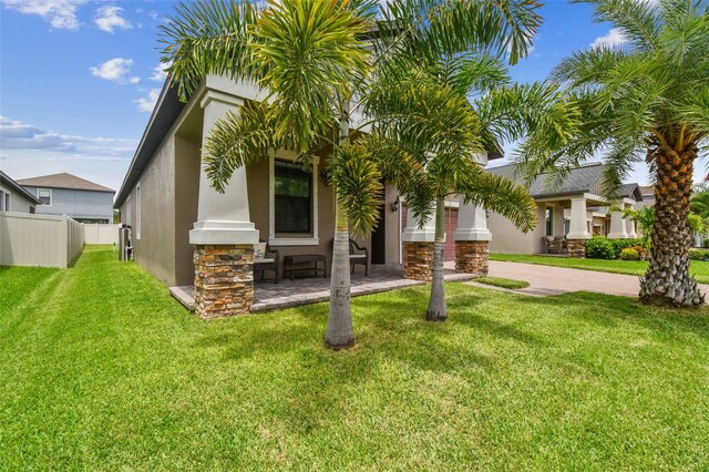 view of front of property featuring stucco siding, stone siding, a front yard, and fence