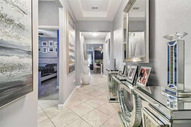 hallway featuring light tile patterned floors, baseboards, a raised ceiling, and visible vents