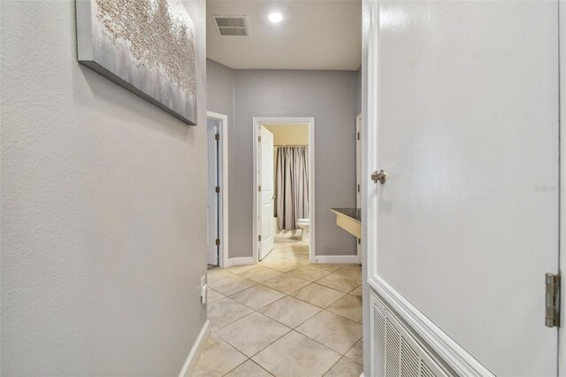 hall featuring baseboards, visible vents, and light tile patterned floors