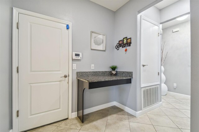 corridor with baseboards, visible vents, and light tile patterned floors