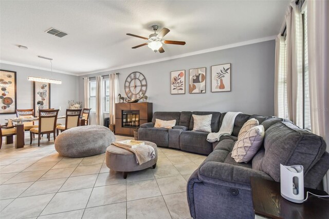 living area featuring light tile patterned flooring, a ceiling fan, visible vents, and ornamental molding