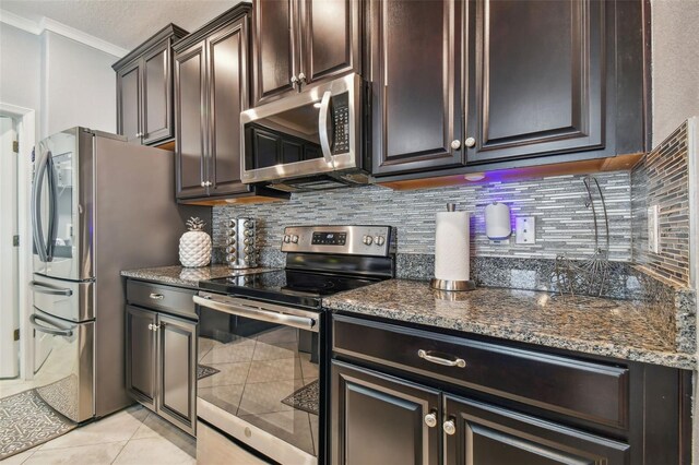 kitchen with crown molding, dark brown cabinetry, appliances with stainless steel finishes, light tile patterned floors, and backsplash