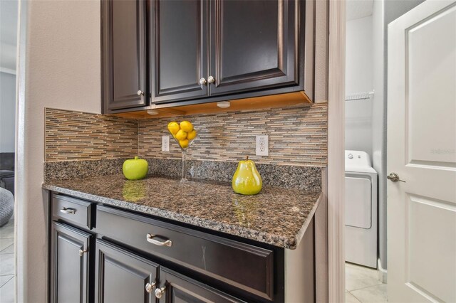kitchen featuring light tile patterned floors, dark stone counters, tasteful backsplash, and washer / clothes dryer