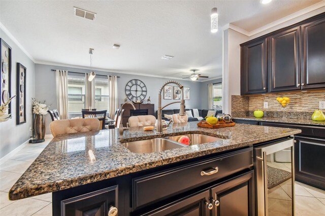 kitchen featuring visible vents, ornamental molding, a kitchen island with sink, light tile patterned flooring, and a sink