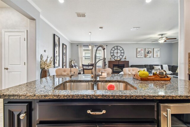 kitchen with visible vents, ornamental molding, a fireplace, open floor plan, and a sink