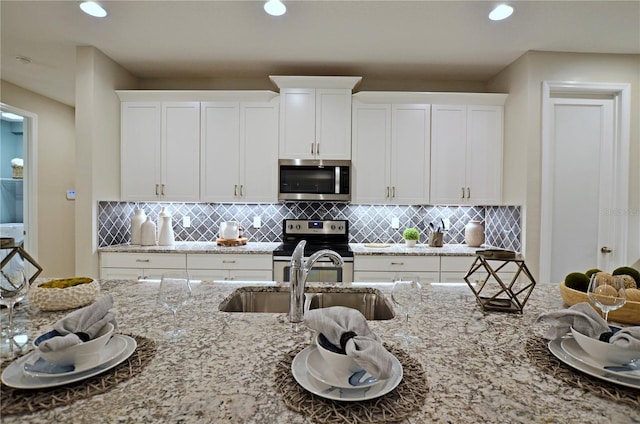 kitchen featuring appliances with stainless steel finishes, light stone countertops, sink, and white cabinets