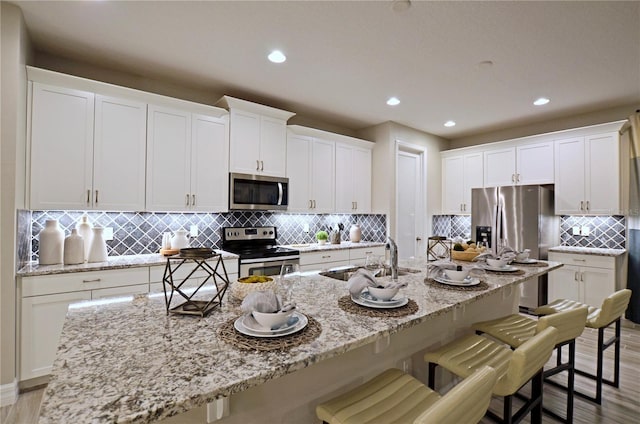 kitchen with stainless steel appliances, a breakfast bar, a center island with sink, and white cabinets