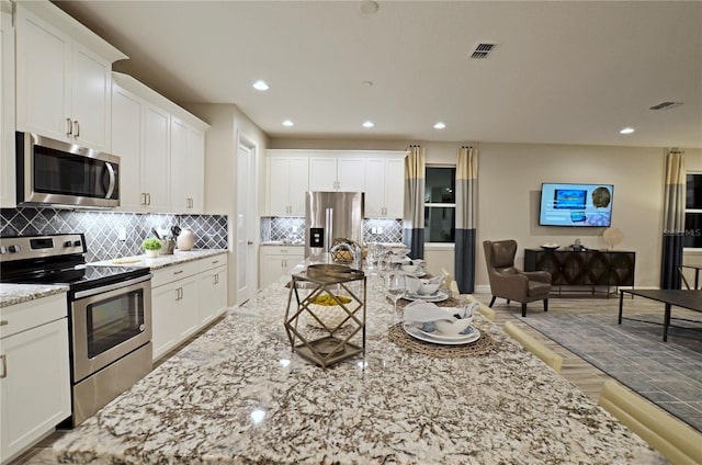 kitchen with sink, appliances with stainless steel finishes, white cabinetry, light stone counters, and tasteful backsplash