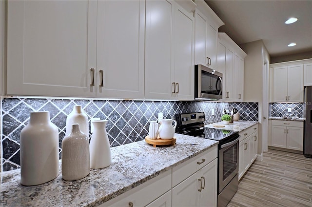 kitchen featuring white cabinetry, backsplash, stainless steel appliances, light stone counters, and light wood-type flooring