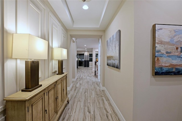 corridor featuring a tray ceiling and light hardwood / wood-style flooring