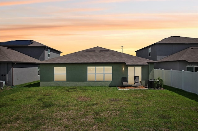 back house at dusk featuring central AC unit and a lawn