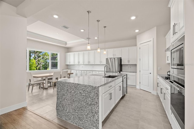 kitchen with stainless steel appliances, light hardwood / wood-style floors, an island with sink, light stone countertops, and white cabinetry