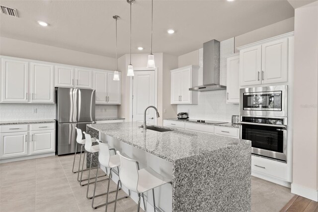 kitchen with a center island with sink, white cabinetry, appliances with stainless steel finishes, sink, and wall chimney exhaust hood