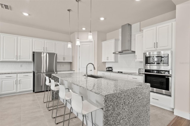 kitchen featuring light stone counters, stainless steel appliances, a sink, white cabinets, and wall chimney range hood