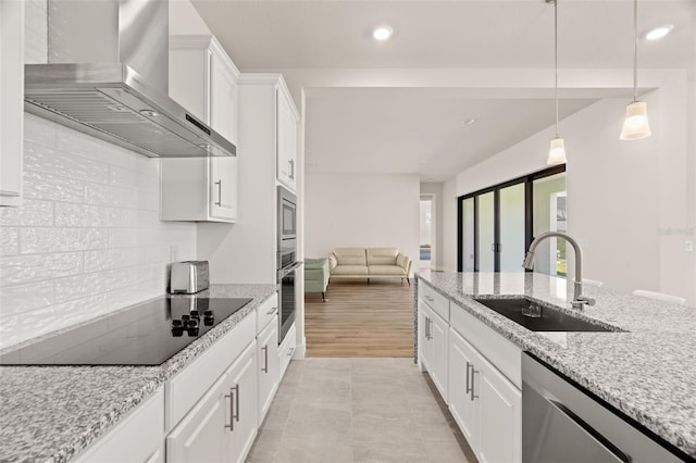 kitchen featuring stainless steel appliances, wall chimney exhaust hood, sink, white cabinetry, and decorative light fixtures