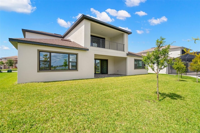 back of property featuring a balcony, a yard, and stucco siding