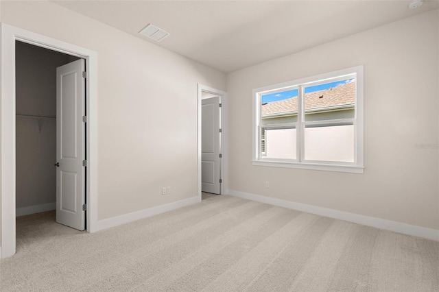 unfurnished bedroom featuring carpet floors, a walk in closet, visible vents, and baseboards