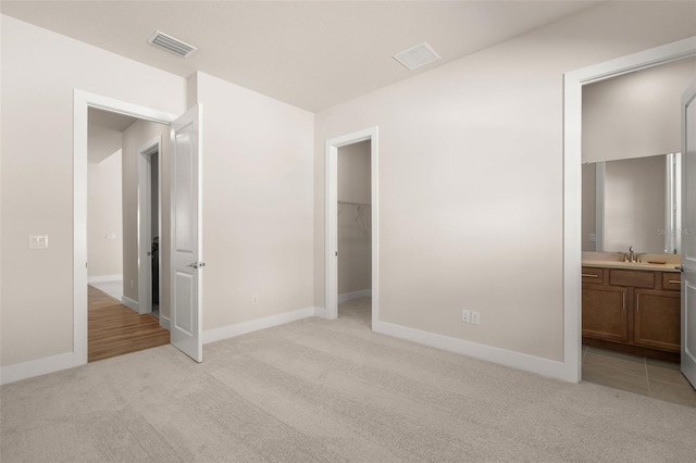 unfurnished bedroom featuring light carpet, sink, ensuite bathroom, a closet, and a spacious closet