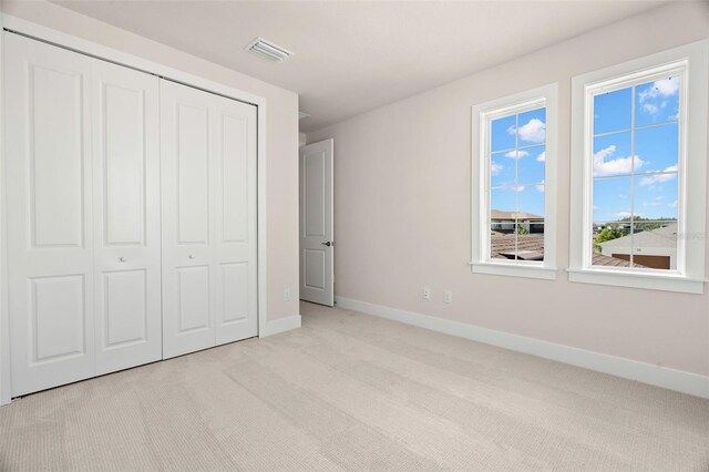 unfurnished bedroom with light colored carpet and a closet