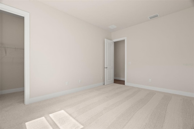 unfurnished bedroom with light colored carpet, a walk in closet, and a closet