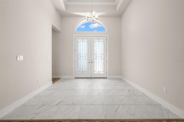 foyer entrance with a tray ceiling, french doors, and a notable chandelier