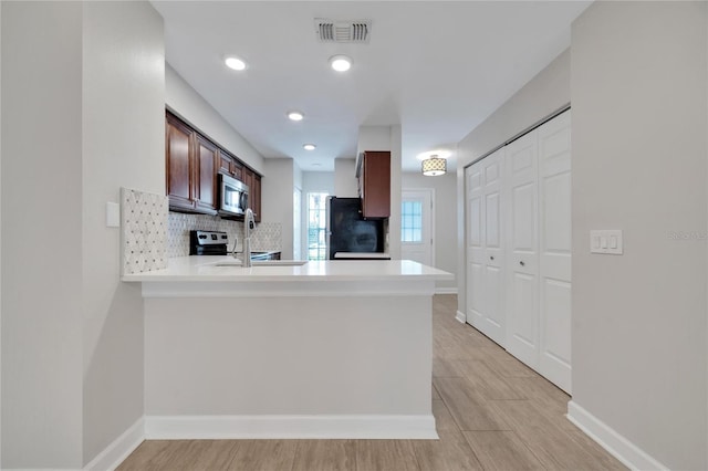 kitchen with sink, appliances with stainless steel finishes, tasteful backsplash, kitchen peninsula, and light wood-type flooring